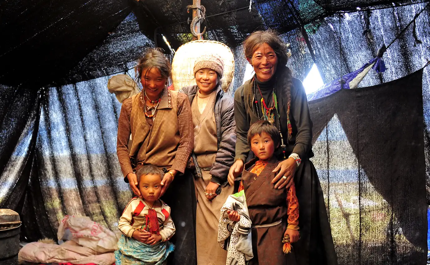 Tibetan nomadic family stands inside a traditional tent on the plateau, sharing a warm moment with visitors during a Tibet adventure tour.