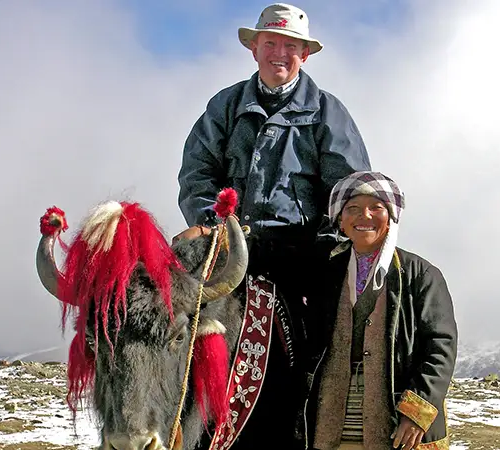 Travelers and a local Tibetan guide with a yak during a rest stop as part of a Tibet acclimatization plan in the high Himalayas.