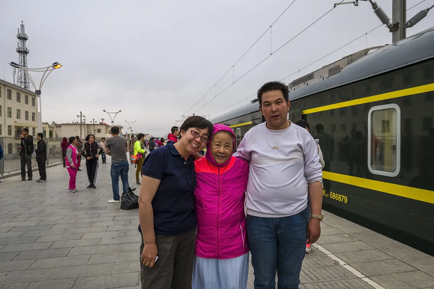 Three travelers stand beside the Tibet train at a station stop, showing a practical overland route often used for solo Tibet travel.