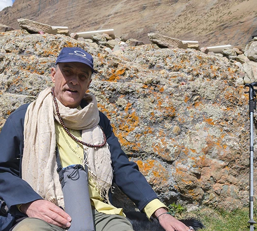 A trekker rests against a rocky hillside with a walking pole. He enjoys a peaceful break during a rewarding and affordable budget Tibet tour.