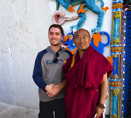 A traveler and a Buddhist monk share a friendly handshake in front of a brightly decorated temple wall. Foreign visitors need a Tibet visa and permits to visit these sacred sites.