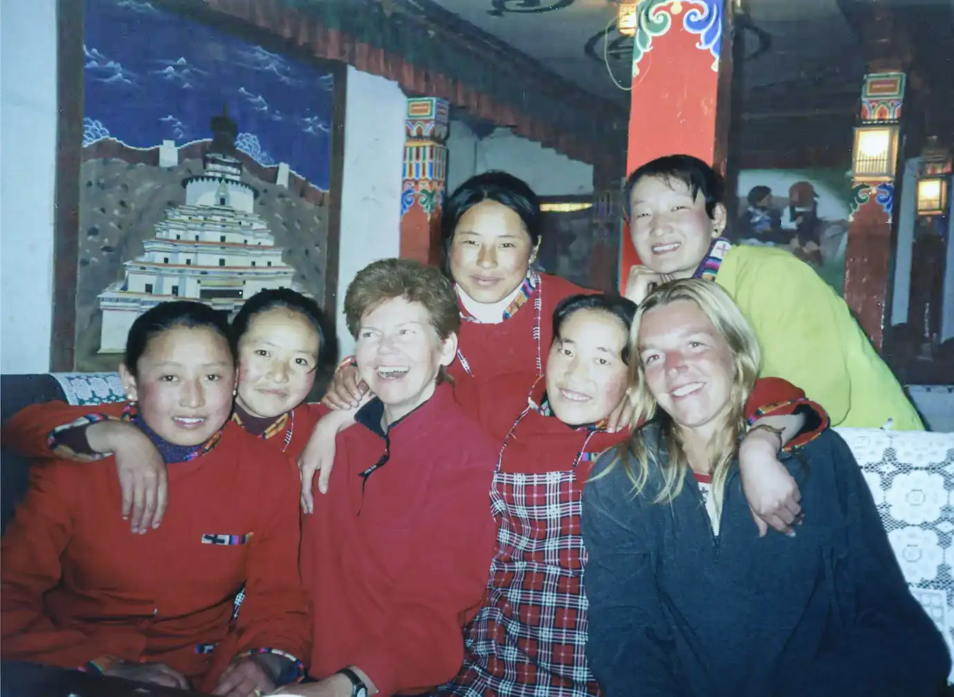 Travelers and local women share a warm cultural moment indoors while planning a Tibet tour experience