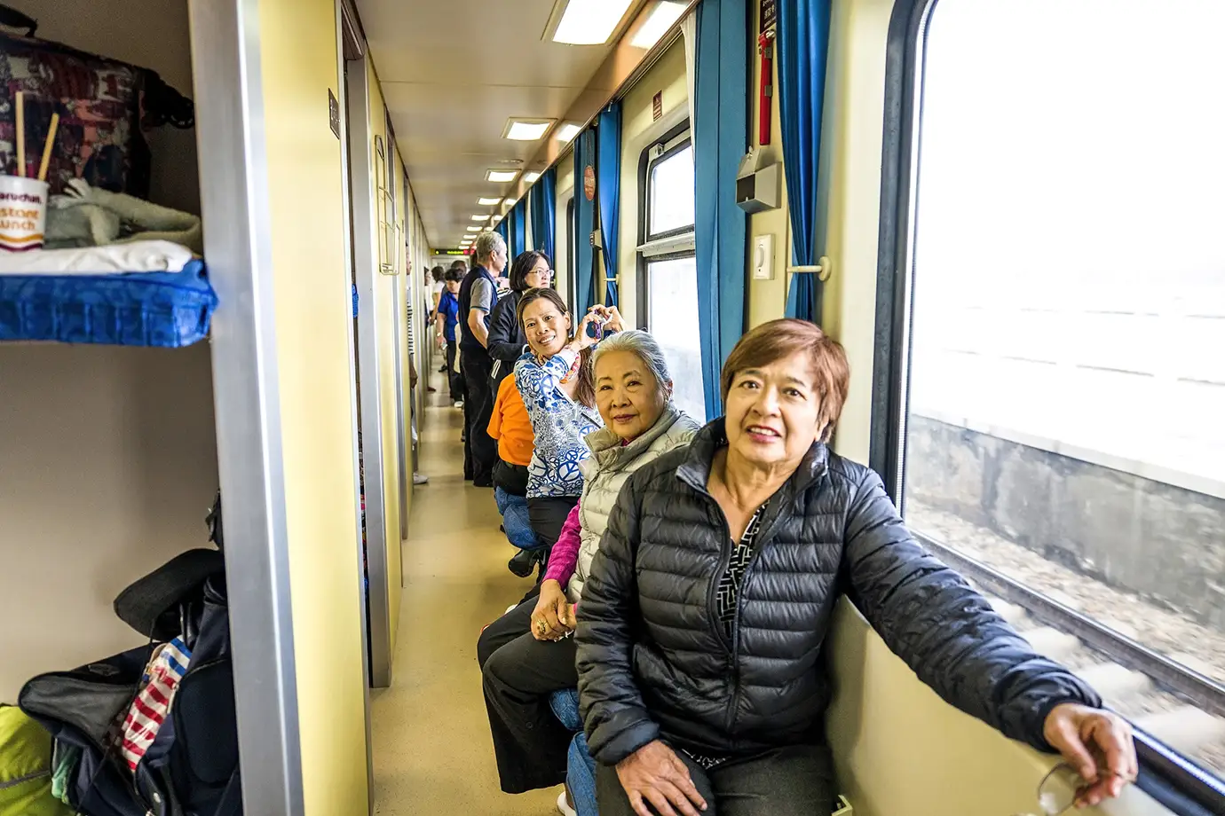 Travelers sit beside large windows inside a high-altitude train cabin during a Tibet tour by train, enjoying scenic views of the Tibetan Plateau along the Qinghai–Tibet Railway.