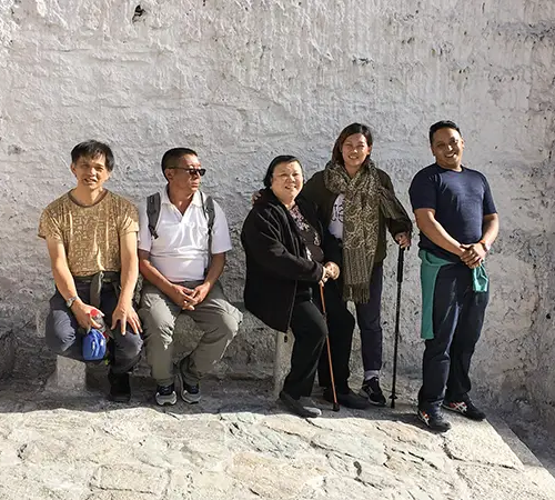 Travelers resting beside a white stone wall during a Tibet Tour Safety-focused cultural visit