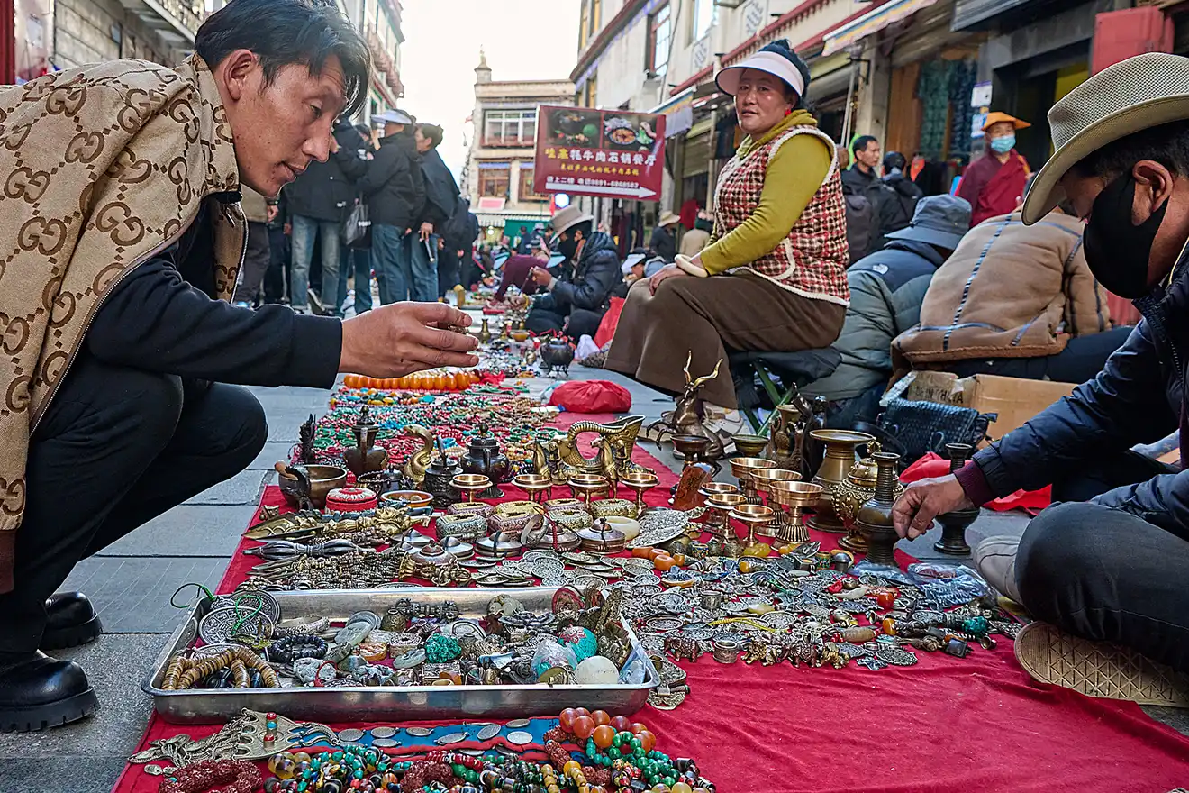 A traveler examines local jewelry and artifacts at an outdoor market in Lhasa. Most visitors must secure a Tibet visa and special permits before exploring these historic stalls.