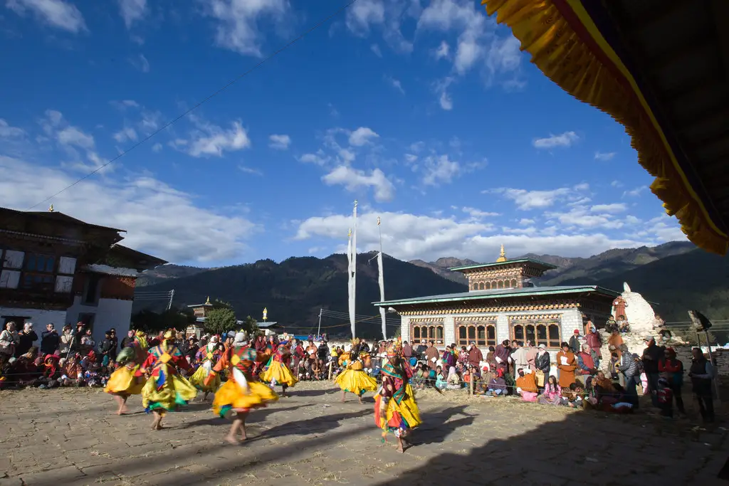 Traditional masked dancers perform during a Tsechu festival celebration at a Bhutan Dzong courtyard, surrounded by local spectators and colorful cultural displays.