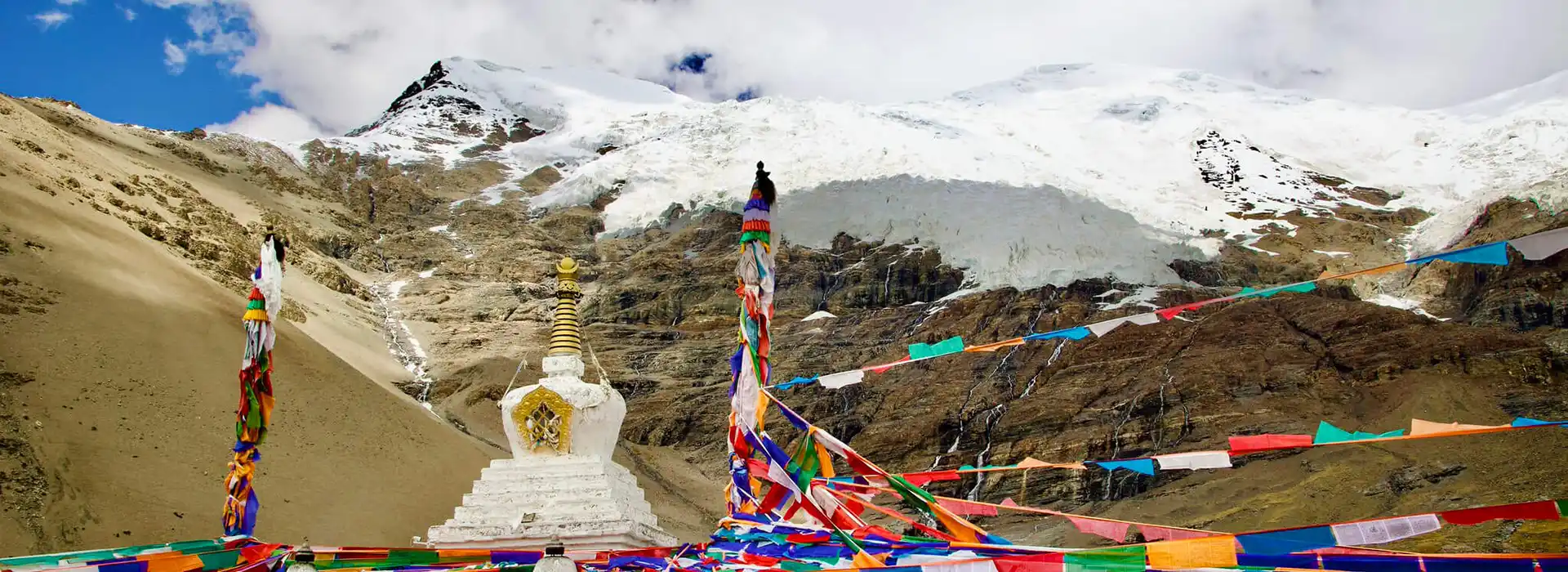 A white Buddhist stupa stands before a massive snow-covered glacier and rocky mountain. This breathtaking view is a highlight of a Tibet tour from the UK.