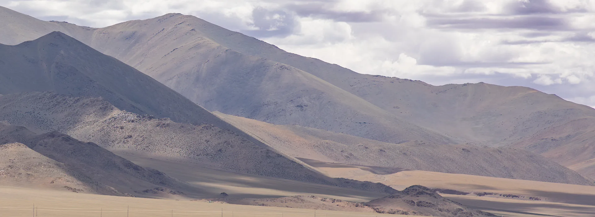 Vast rolling mountains stretch across the horizon under a cloudy sky. These dramatic landscapes change appearance based on the Tibet weather by month.