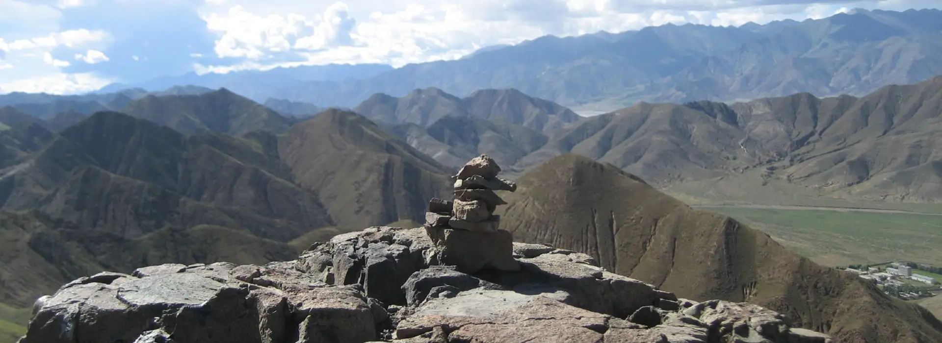 A rocky summit above broad mountain ridges and a distant valley shows the quiet landscapes travelers may encounter during solo Tibet travel in higher regions.