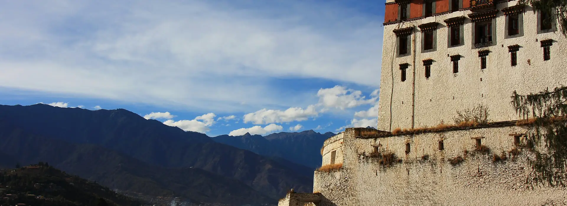 View from Tashichho Dzong overlooking mountain valleys and Himalayan landscape, showing the massive white walls of a historic Bhutan Dzong fortress in Thimphu.