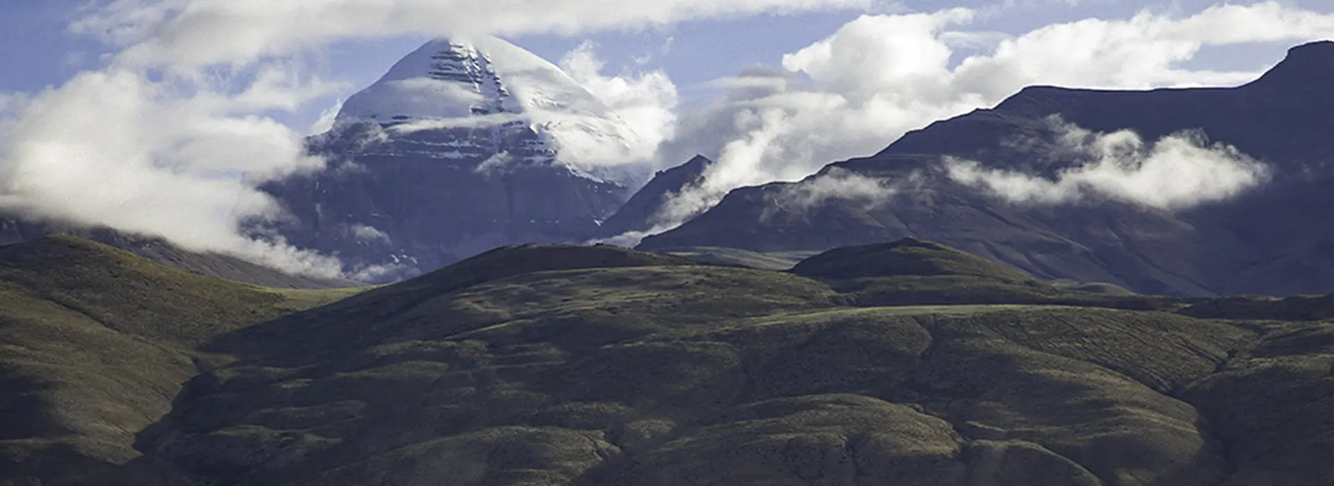 A snow-covered mountain peak rises above rolling hills and a sea of clouds. Travelers must obtain a Tibet visa and specialized entry permits to view these remote landscapes.