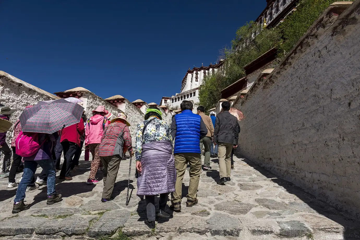 Travelers walk up the stone path toward Potala Palace in Lhasa, showing a major stop many visitors reach after learning how to get to Tibet.