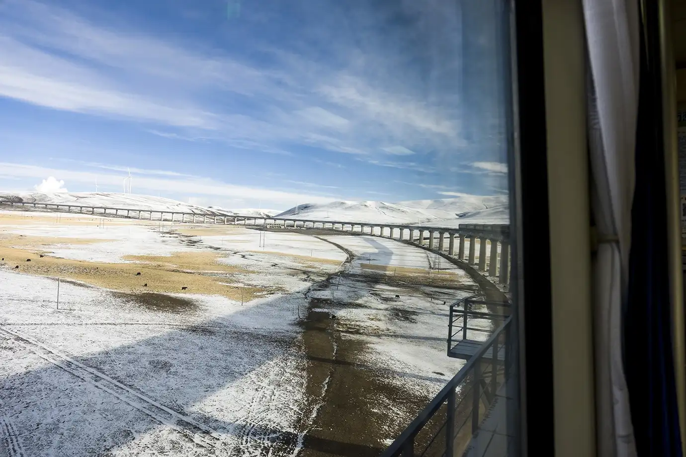 A snowy plateau and long railway bridge stretch across the landscape, showing a scenic part of the route many travelers see when learning how to get to Tibet.