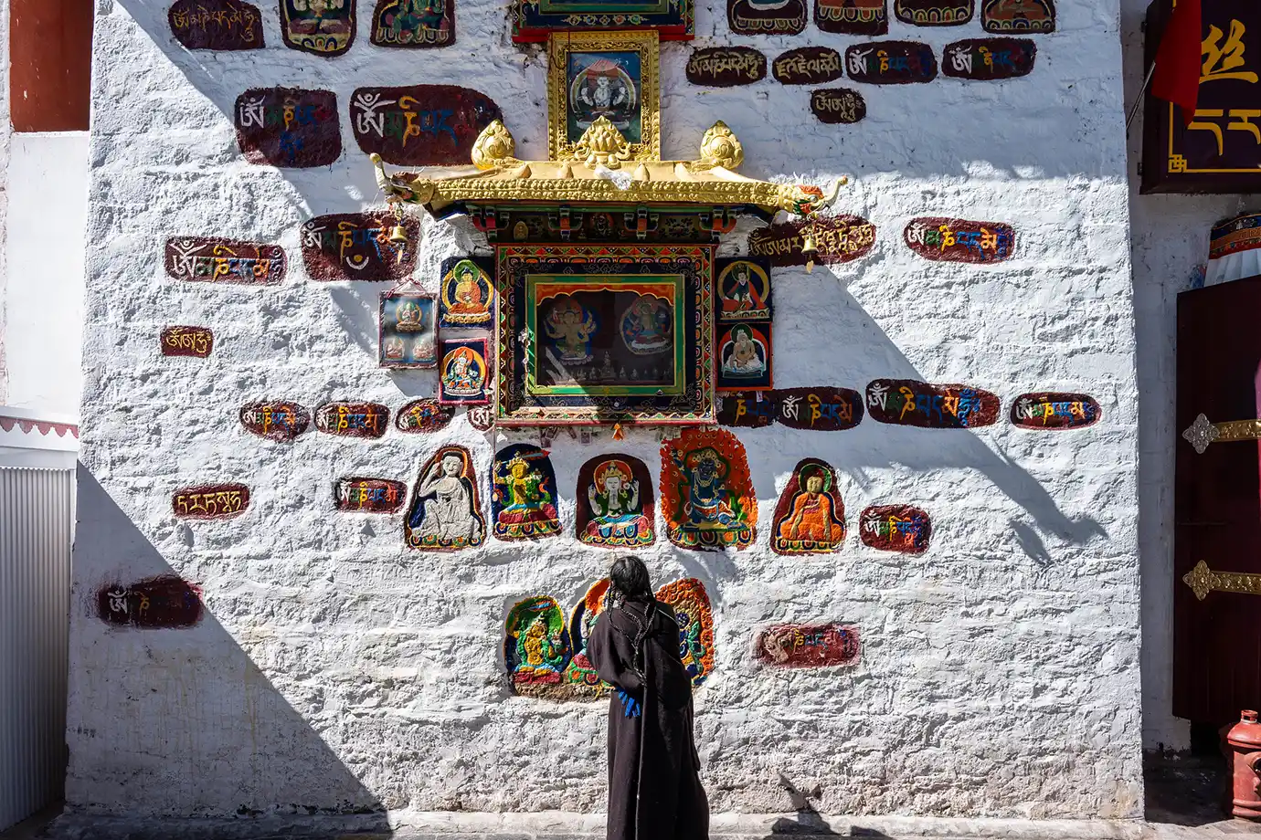 A woman in traditional Tibetan clothing views colorful religious murals and mantras carved into a white stone wall, a serene stop on a Tibet tour itinerary for first-time visitors.