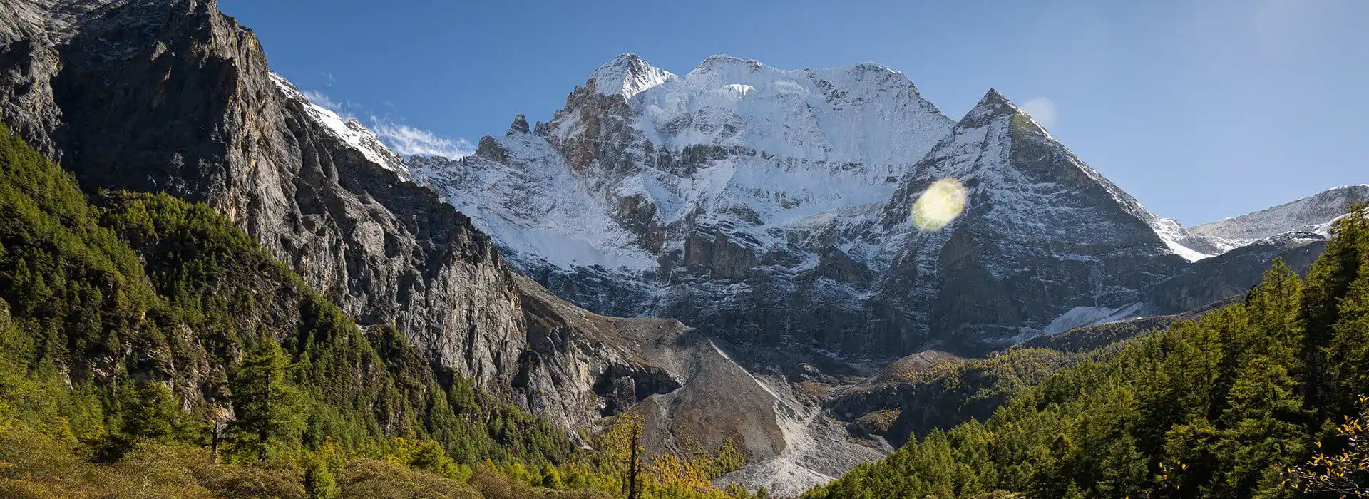 Snow-capped mountain peaks tower over a lush green forest valley in the Himalayas. This scenic route is accessible for travelers holding an Everest Base Camp Tibet permit.