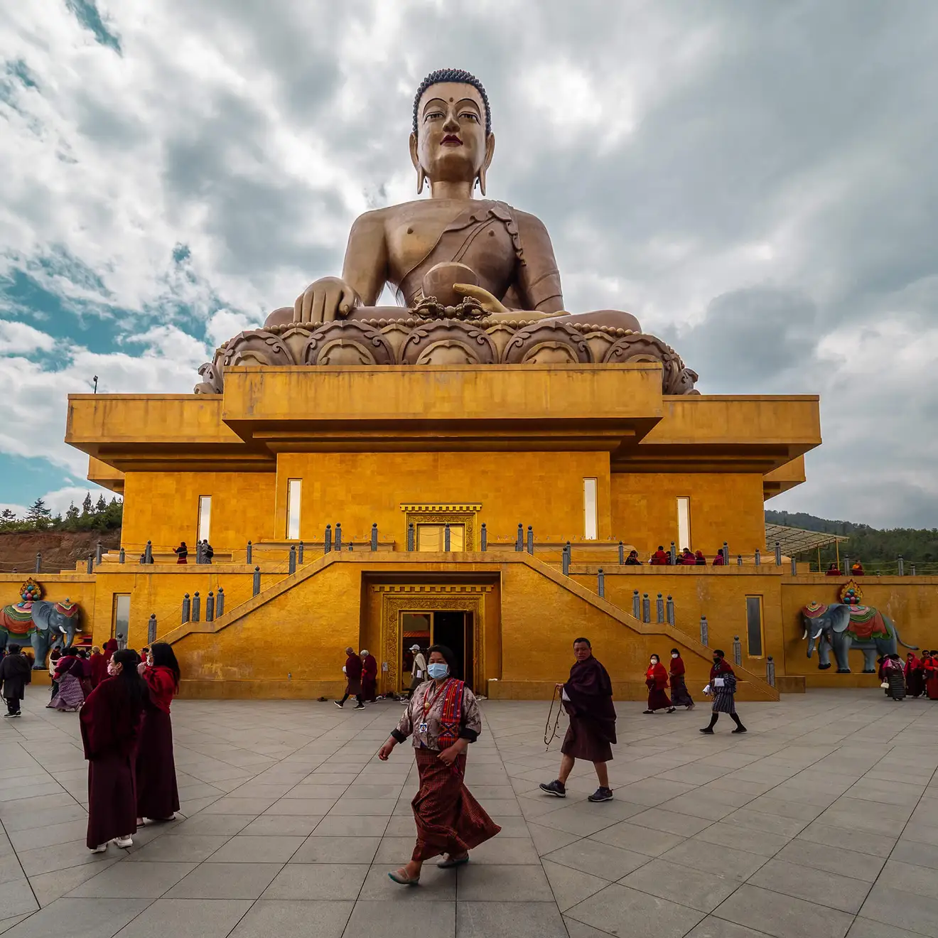 The large golden Buddha Dordenma statue in Thimphu, Bhutan, looms over a wide courtyard filled with local people during an Essential Bhutan Travel Tour.