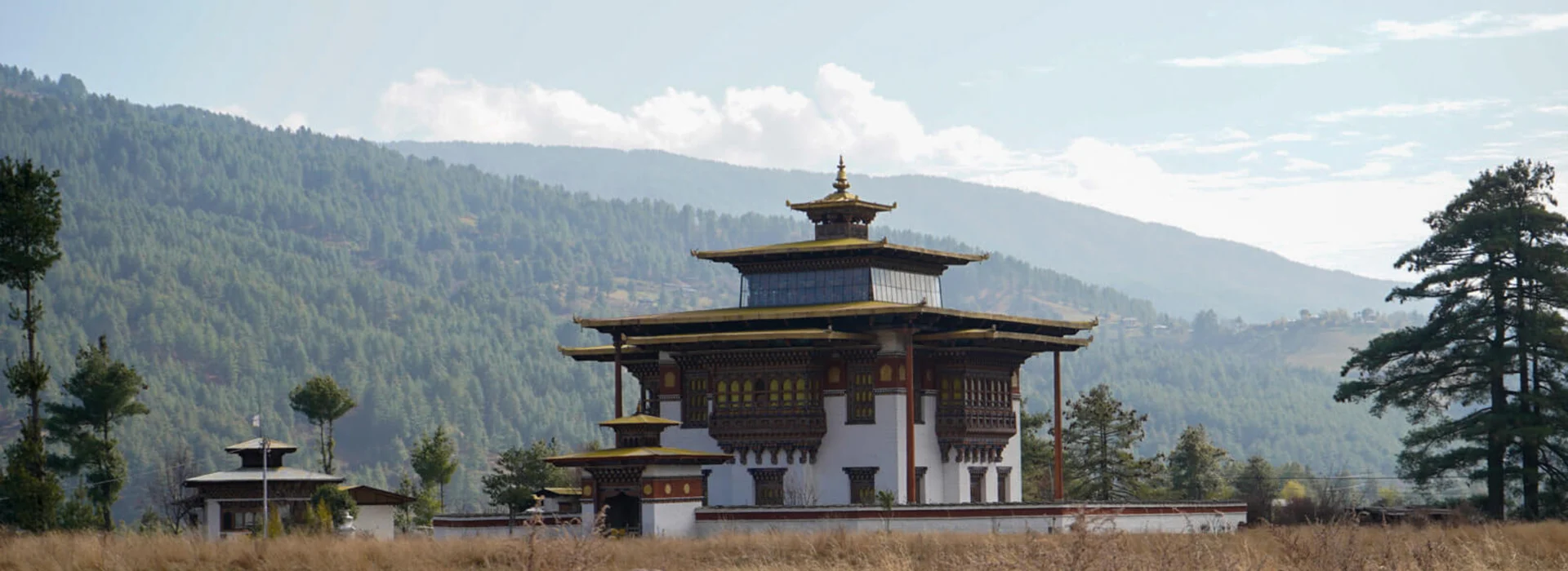 A man wearing a warm blue jacket stands before a large, vibrant Bhutanese painting of a protective deity during a specialized Bumthang Cultural Trek and Tour.