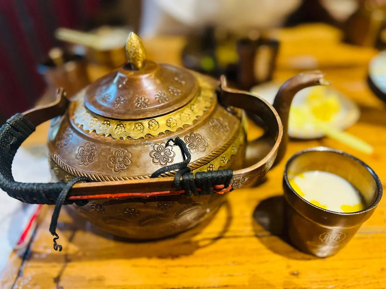 An ornate copper teapot sits next to a cup of creamy yak butter tea, a quintessential staple of authentic Tibetan food and hospitality.