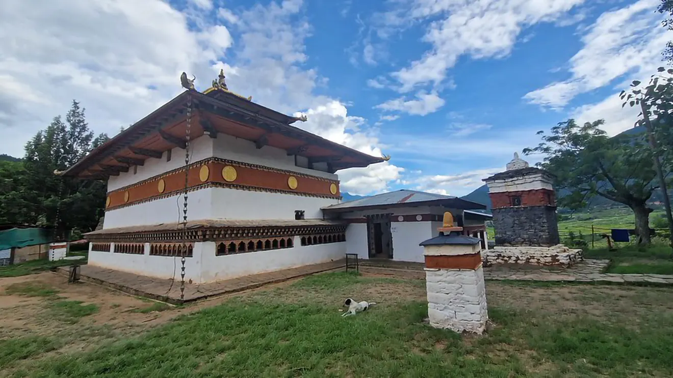 The Chimi Lhakhang temple stands under a bright blue sky with white clouds. This sacred site is a key stop during a Western Bhutan Exploration.
