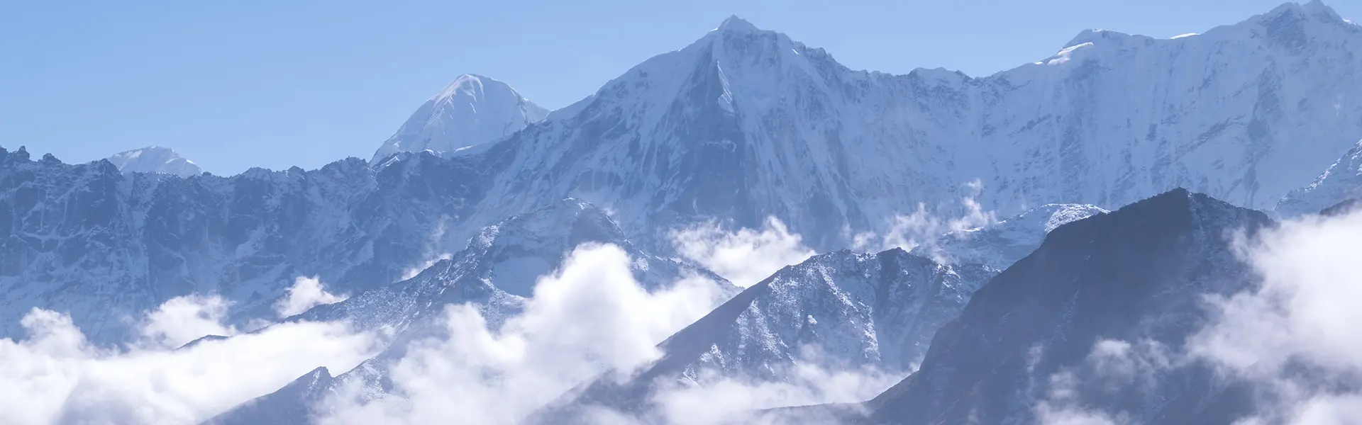 A wide panoramic shot of towering, jagged snow-capped Himalayan mountains rising above a thick layer of white clouds during an Everest Three Passes Trek.