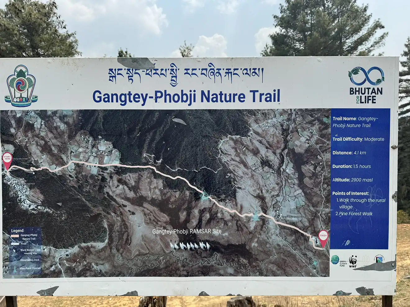 A large informational sign displays a map and trail details for the Gangtey-Phobji path. This map guides visitors during a Phobjikha Valley Nature Tour.