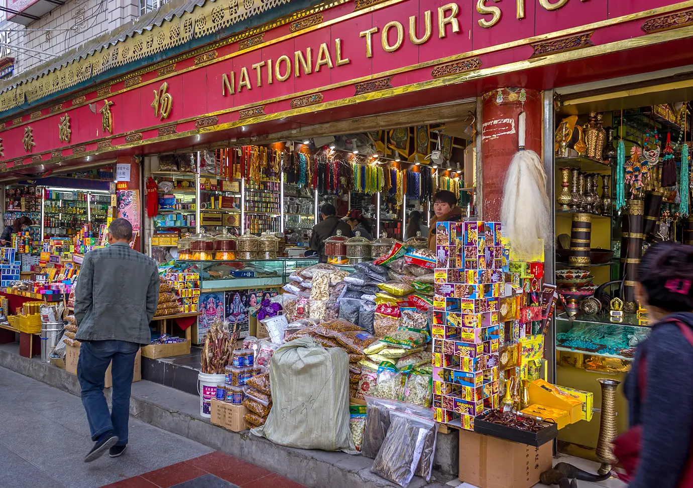 Busy souvenir shop in Lhasa with colorful prayer items, incense, ritual objects, and local products displayed at the storefront.