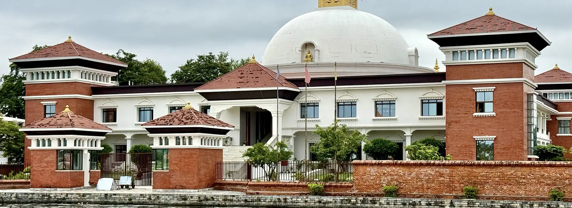 Red brick and white modern buildings surround a large white stupa dome at the Lumbini monastic zone, a peaceful stop during a 10-Day Nepal Itinerary.