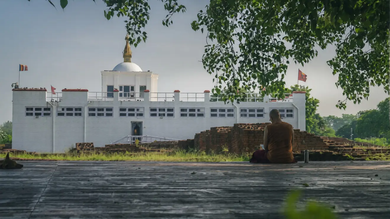 A monk sits in meditation before the sacred white Maya Devi Temple and ancient ruins. This peaceful scene is a highlight of any Lumbini Travel Guide.
