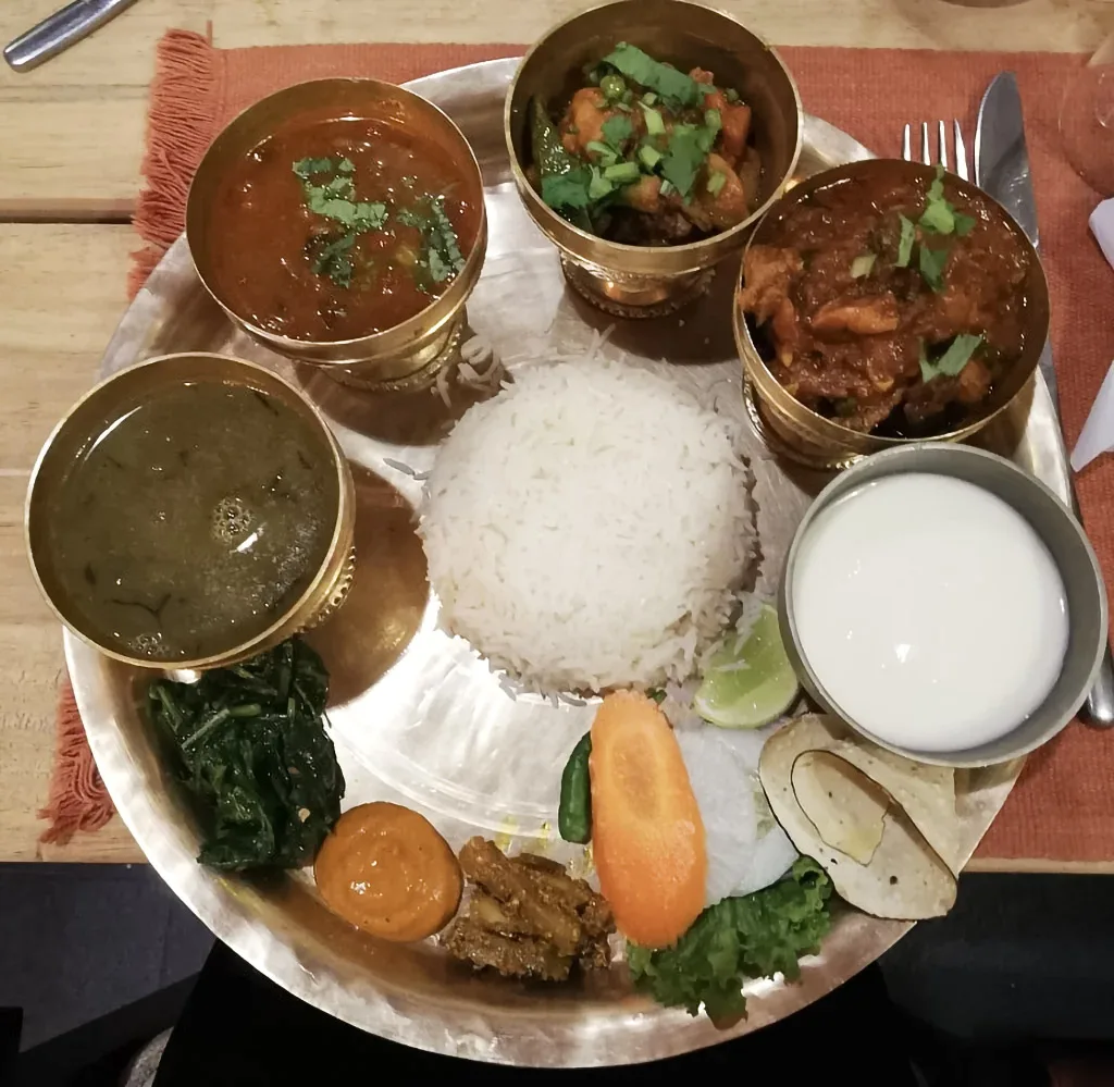 A traditional Nepali thali set features rice, lentil soup, and various vegetable curries served on a brass plate, an essential meal noted in any Nepal Travel Budget Guide.