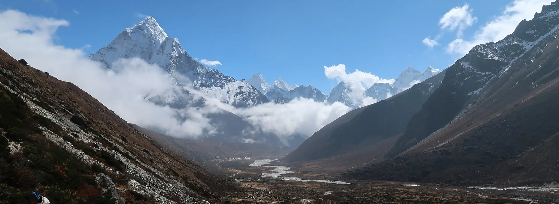 A sweeping mountain valley view featuring Ama Dablam and other snow-dusted peaks under a clear blue sky, highlighting scenic things to do in Nepal.
