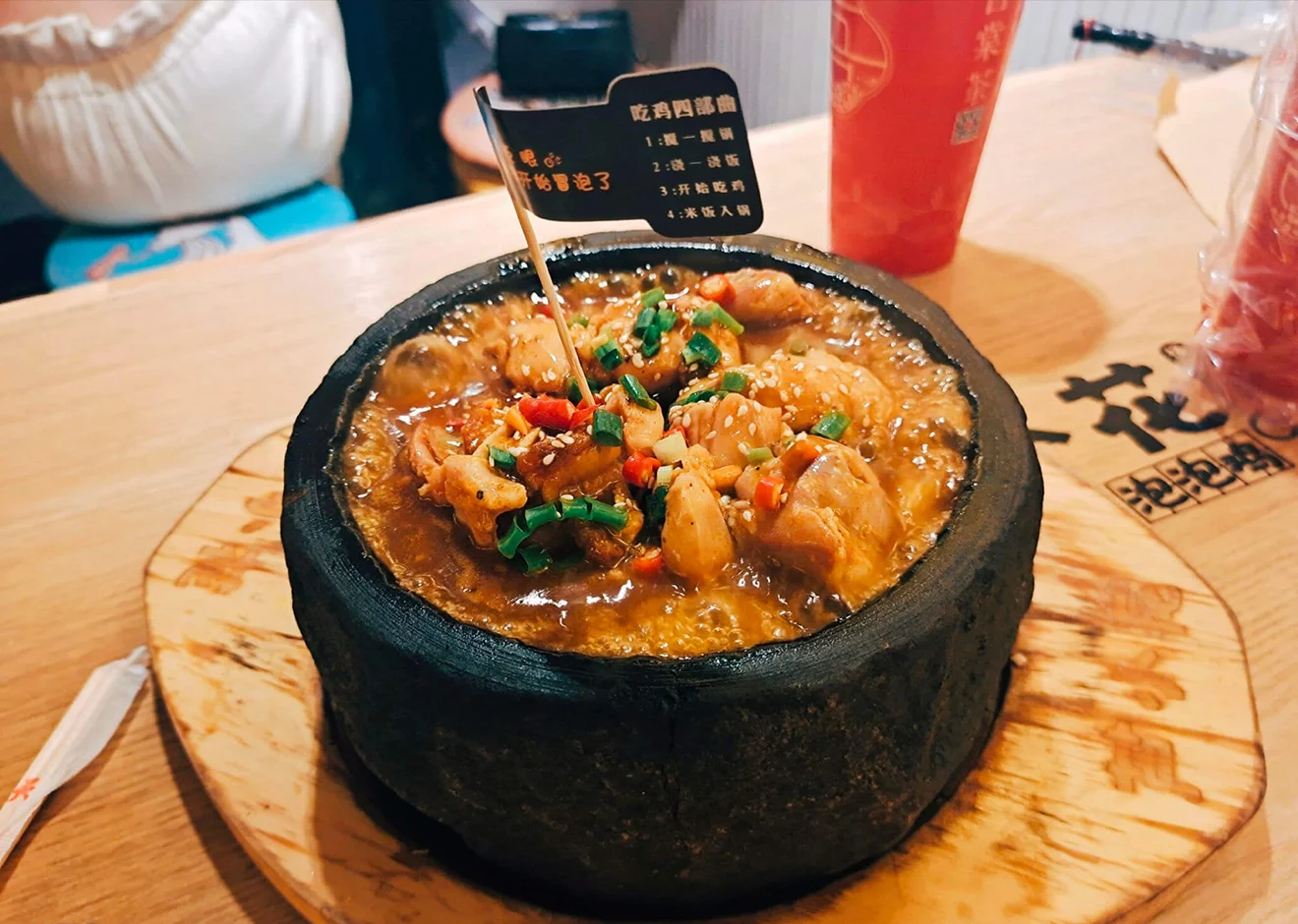 A bubbling Nyingchi stone pot chicken stew topped with fresh scallions and chili peppers, showcasing a famous specialty of Tibetan food in a rustic setting.
