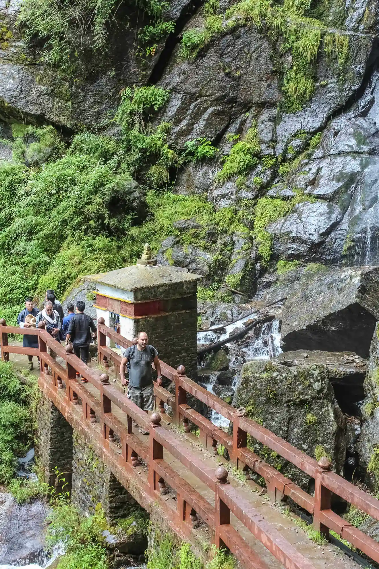 Travelers cross a wooden bridge over a rocky mountain waterfall during an excursion that can be part of a Bhutan bird watching tour.