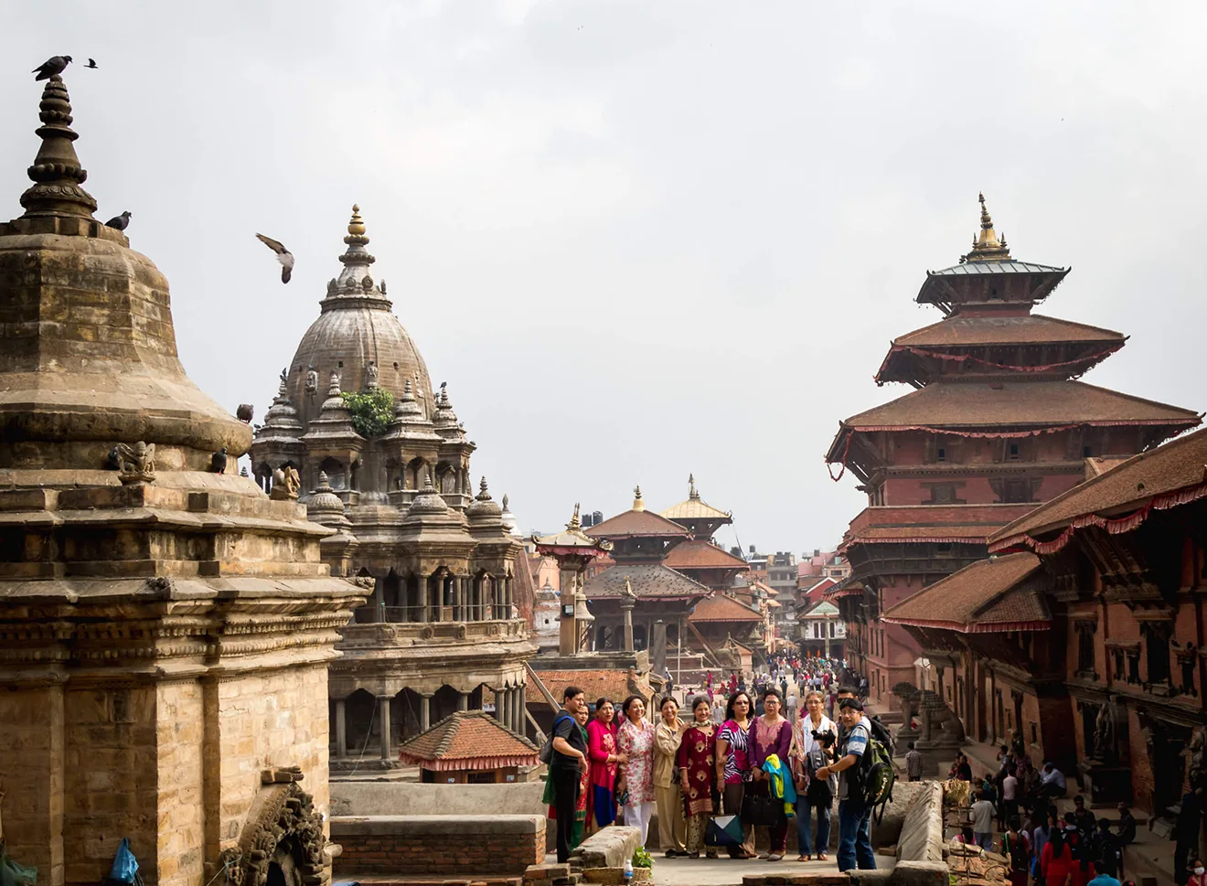 A diverse group of friends smiling and posing for a group photo in Kathmandu's Patan Durbar Square, highlighting it as one of the best cities to visit in Nepal.