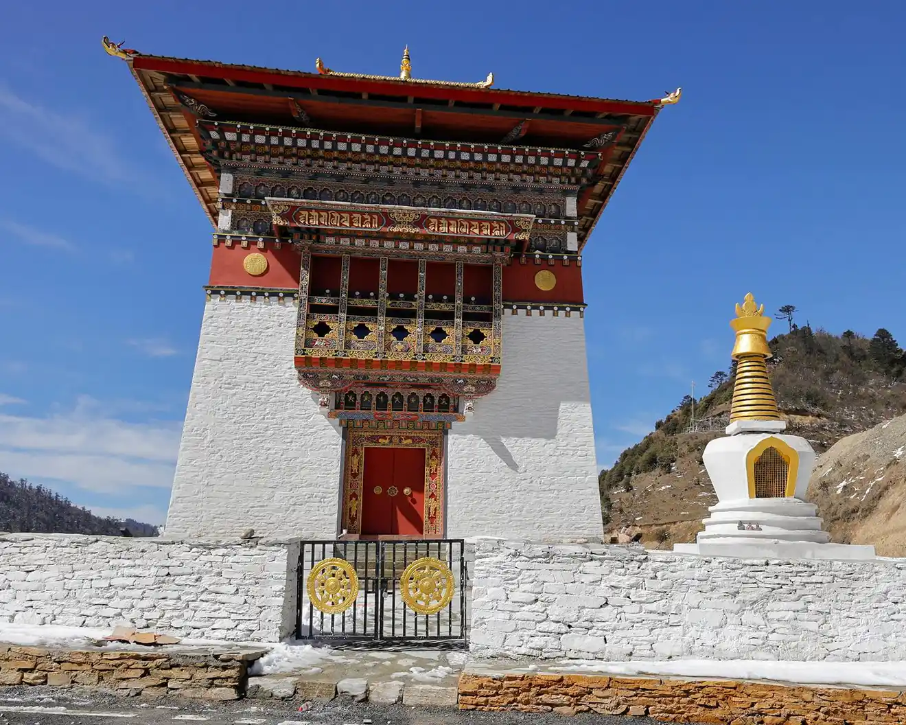 A man stands amidst colorful prayer flags at Pele La Pass in the Himalayan mountains, a key stop on an authentic Bhutan Cultural Tour.