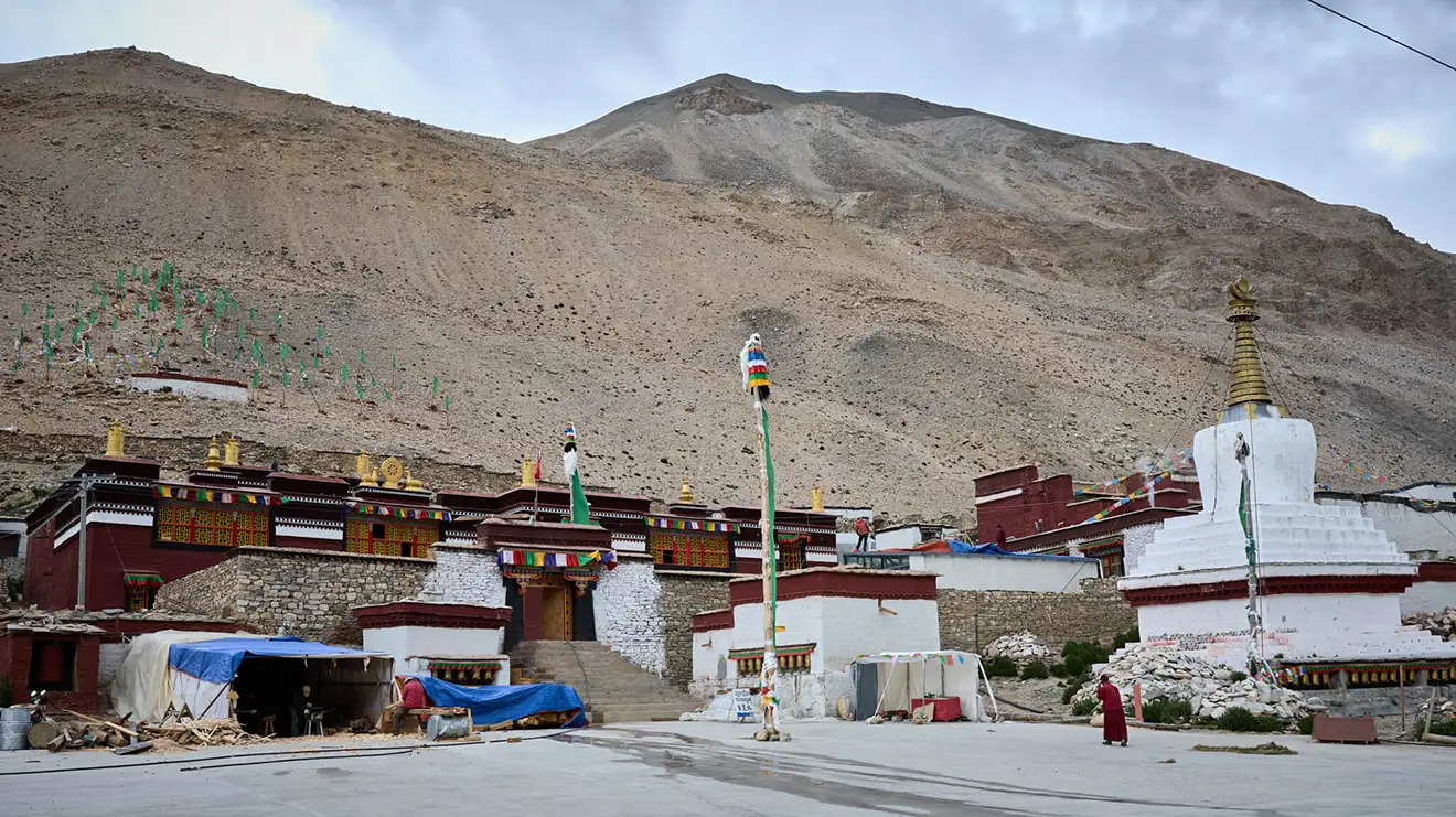 Traditional red and white buildings of Rongbuk Monastery sit beneath a vast mountain. Travelers visit this site while carrying their Everest Base Camp Tibet permit for entry.