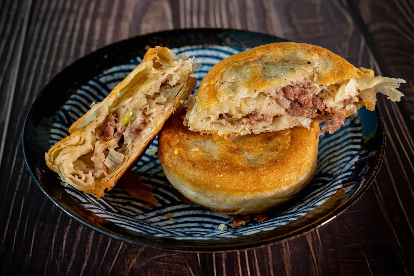 Three golden fried Sha Phaley meat pies served on a blue patterned plate, showing the savory beef and cabbage filling of this popular Tibetan food.