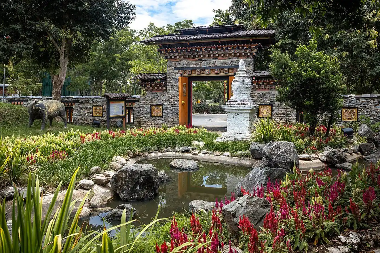 A traditional stone entrance gate and white stupa overlook a garden pond with red flowers at the Royal Botanical Park during a Bhutan Botanical Tour.