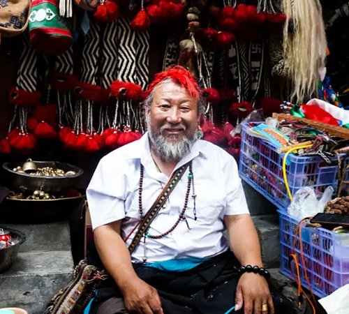 A smiling Tibetan shop owner holds a colorful textile in her traditional store. She offers authentic items for travelers deciding what to buy in Tibet.