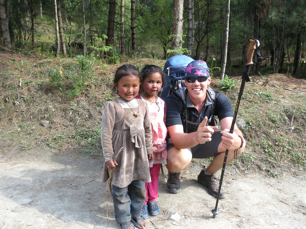 Trekker posing with two local children on a forest trail in Nepal during a Himalayan trekking route
