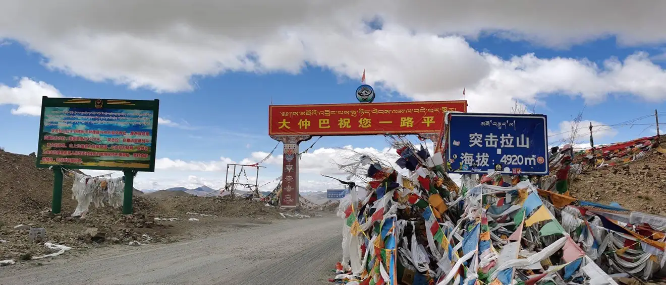 A blue road sign marks Tuji La Pass at 4920 meters high. Colorful prayer flags and a red welcome gate stand along the route toward Everest Base Camp Tibet permit regions.