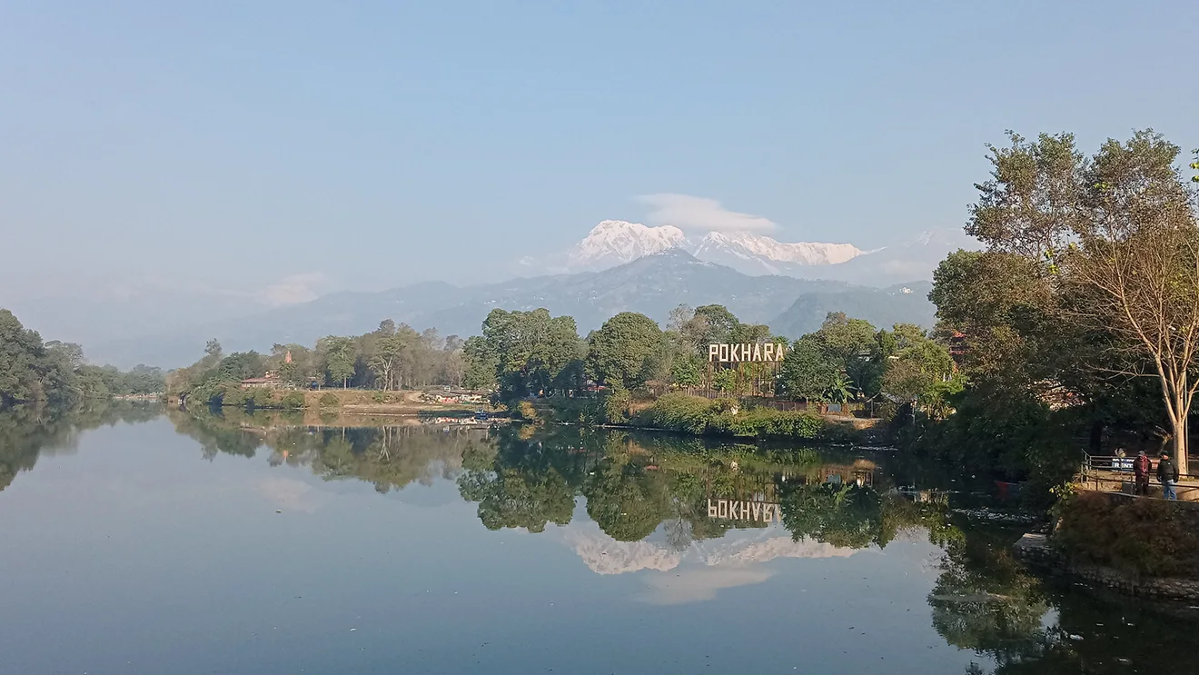 The reflective Phewa Lake in Pokhara perfectly mirrors the distant snow-capped Machhapuchhre peak and the large "POKHARA" sign, a must-visit among Nepal bucket list destinations.