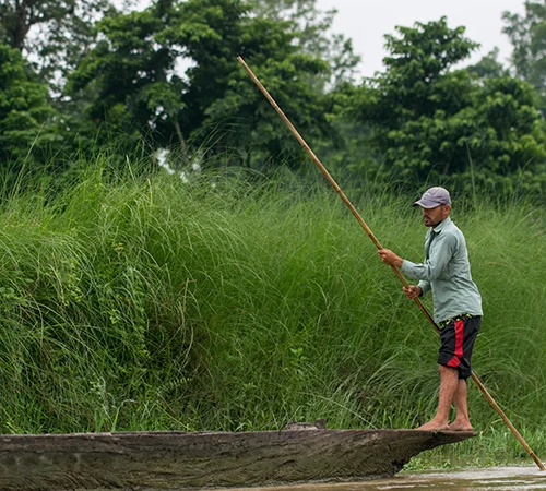 A skilled guide steers a traditional dugout canoe along the Rapti River, showcasing authentic water safaris as top things to do in Chitwan.