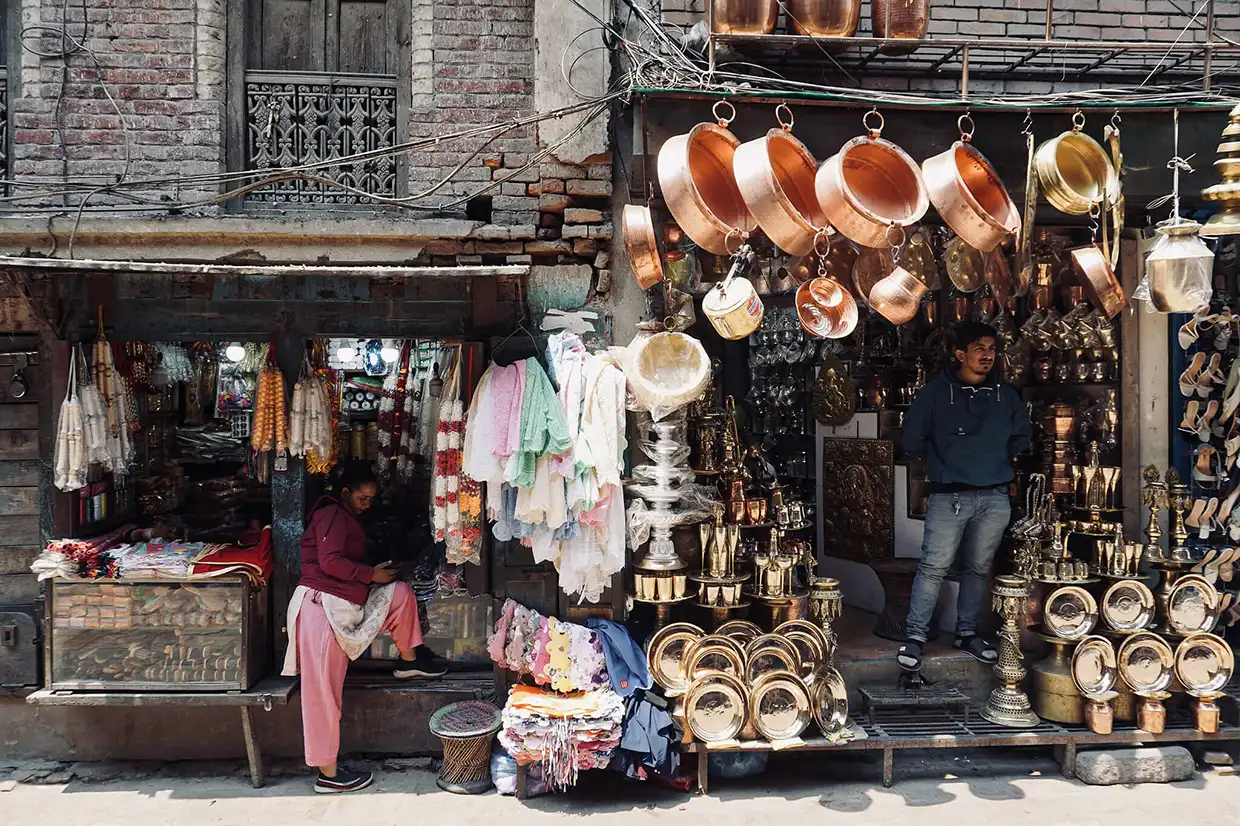 A vibrant street market scene in Nepal showing authentic brass and copper ware, fabric goods, and local shopkeepers, representing some cultural things to do in Kathmandu.
