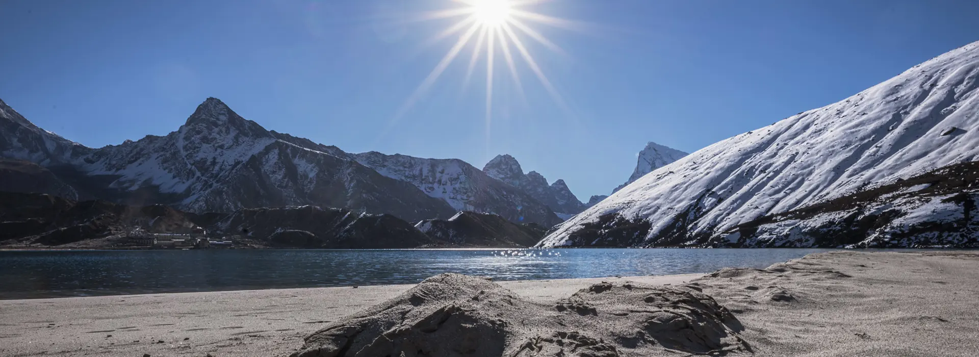 The serene turquoise Gokyo Lake surrounded by massive, snow-capped peaks under a bright sun, a prime example of the best mountain destinations in Nepal.