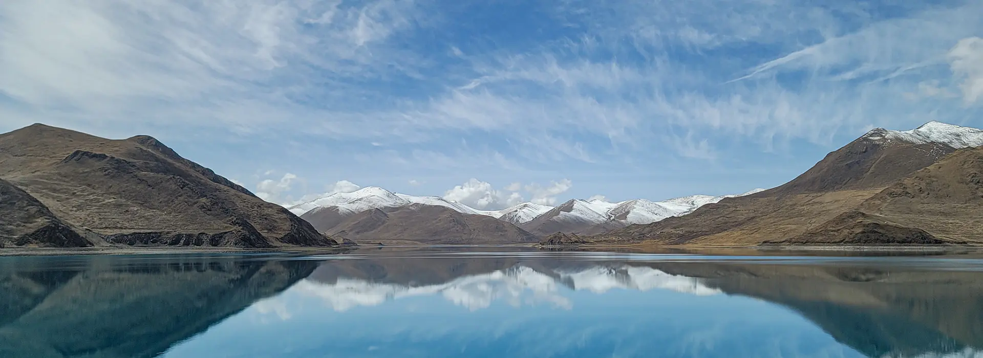 The serene, mirror-like Yamdrok Lake perfectly reflects the surrounding snow-capped peaks. Understanding all Tibet Tour Requirements ensures a smooth, stress-free journey to this breathtaking region.