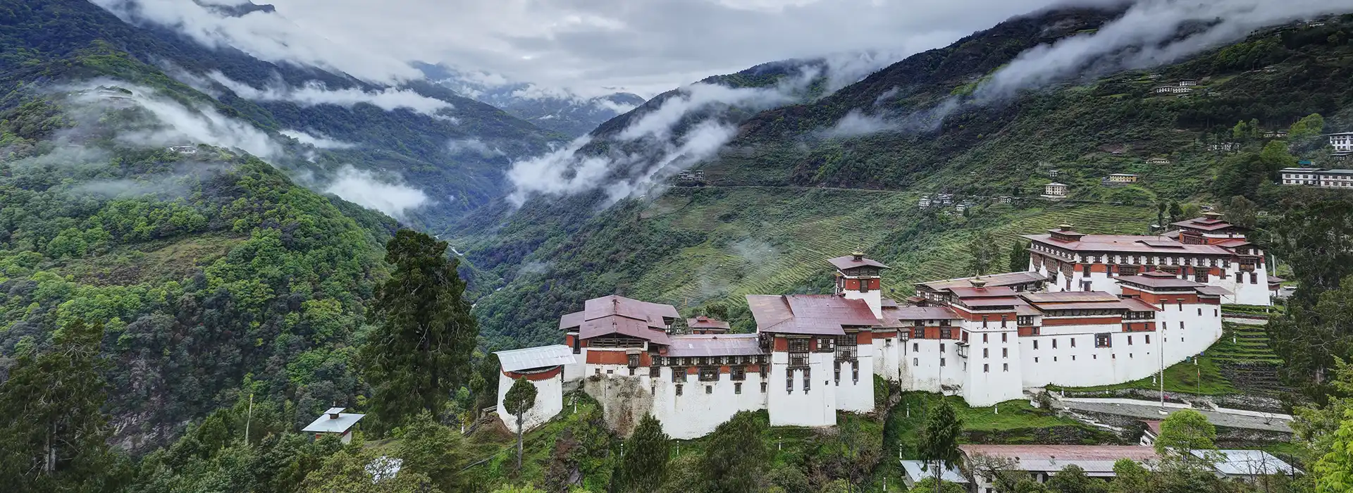 A wide view shows the grand Trongsa Dzong fortress perched on a mountain ridge above a deep valley during a professional Bhutan Highlights Tour.