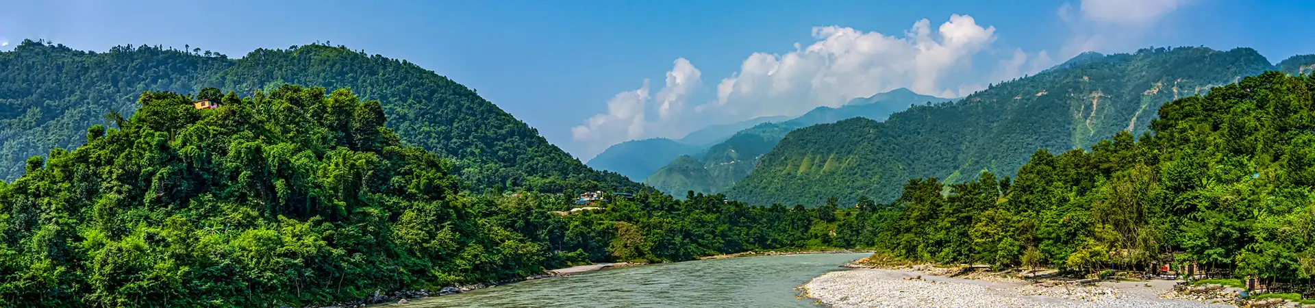 A panoramic view shows a wide river flowing through lush green hills under a bright blue sky. This scenic landscape is a highlight for travelers on a 7-Day Nepal Itinerary.