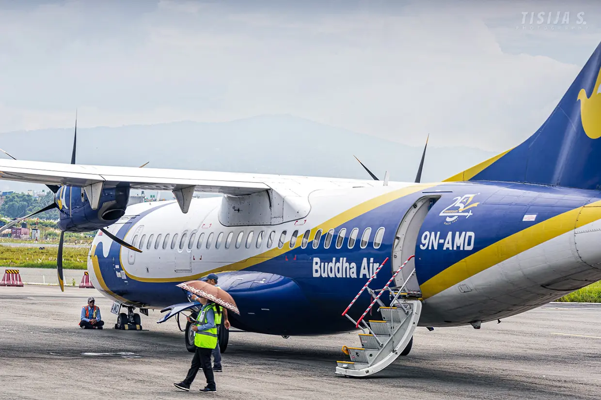 Ground crew members prepare a Buddha Air domestic airplane for passengers on a sunny tarmac. Internal flights are a major component of a Nepal Trip Planning Guide.
