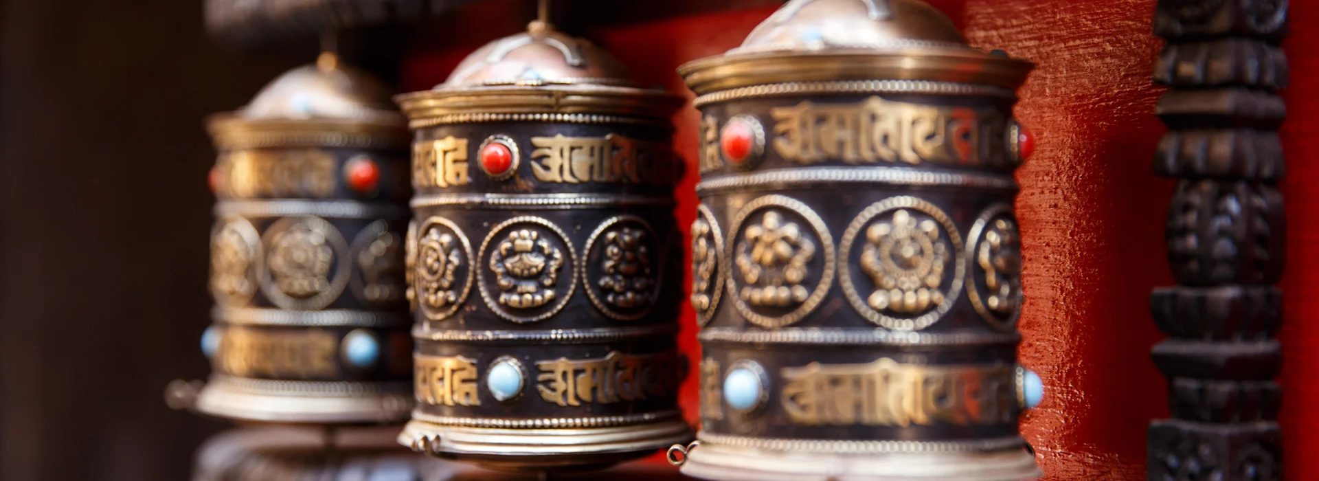 A row of traditional metal prayer wheels with red and turquoise stones stands ready for visitors who explore local temples after enjoying authentic Tibetan food.