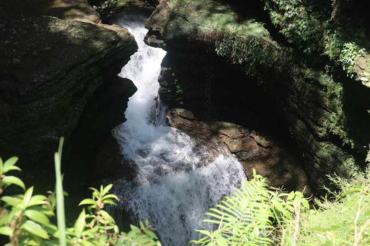 Lush green foliage surrounds the rocky opening to Gupteshwor Mahadev Cave, one of the best places to visit in Pokhara for its underground waterfall.